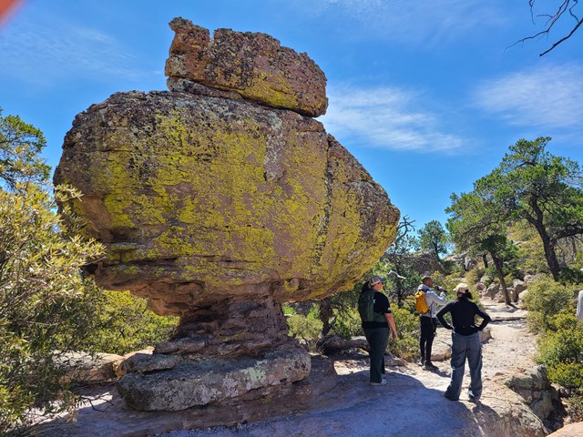 Hikers stand under huge yellow rock that resembles a submarine