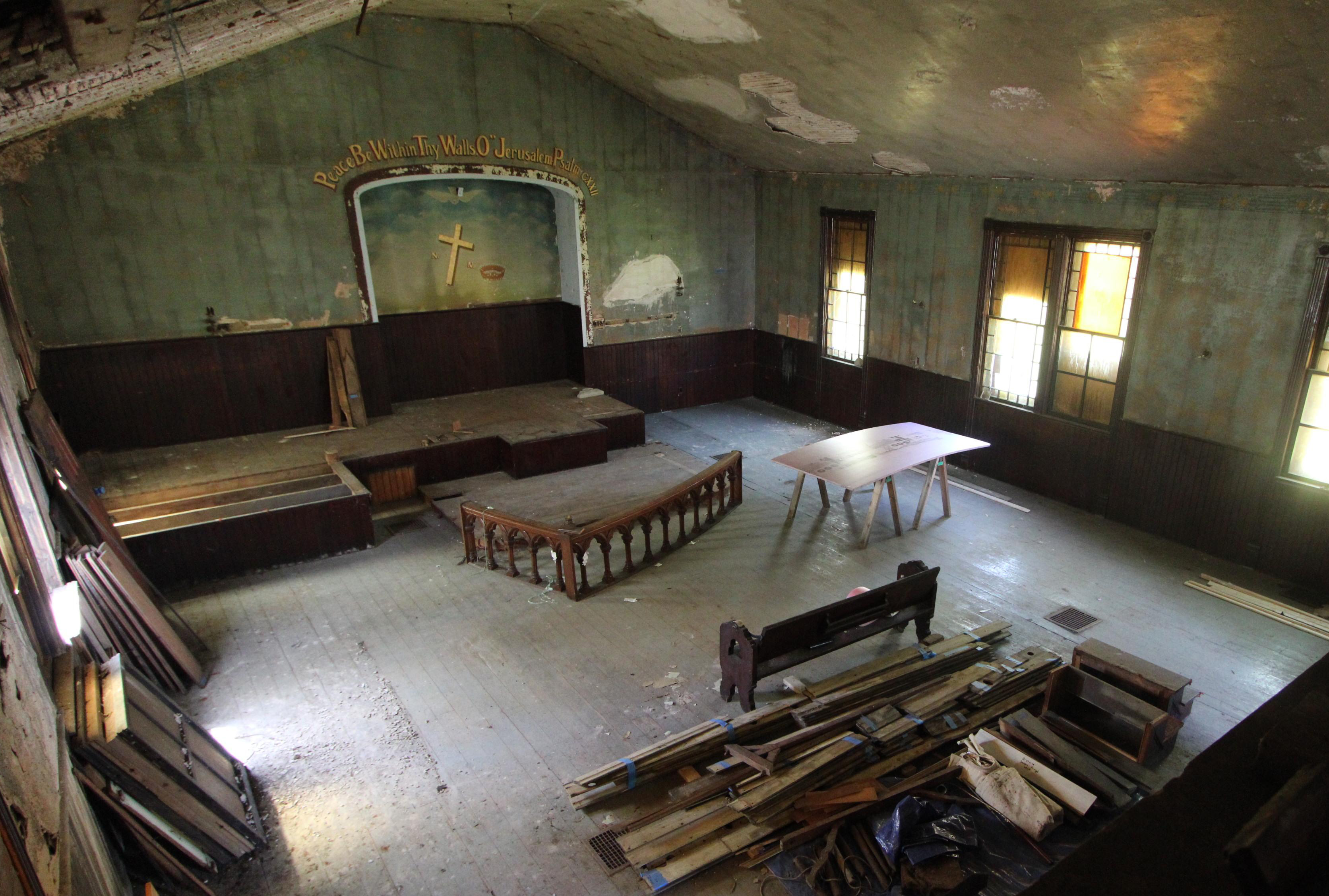 The interior of a run-down church, showing crumbling plaster, boarded windows, and construction materials.