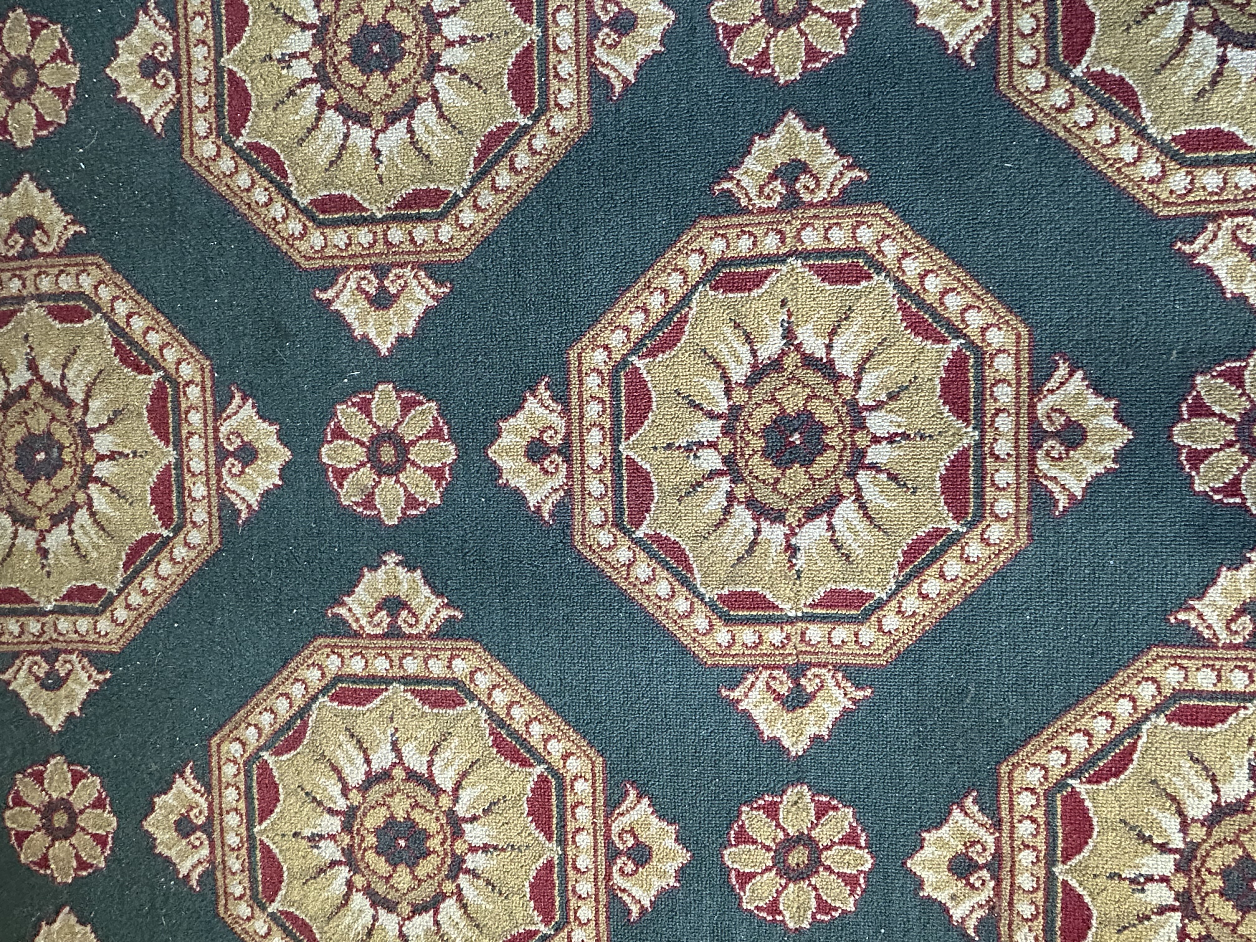 A close up of faded carpet with a green background and gold and red geometric pattern.