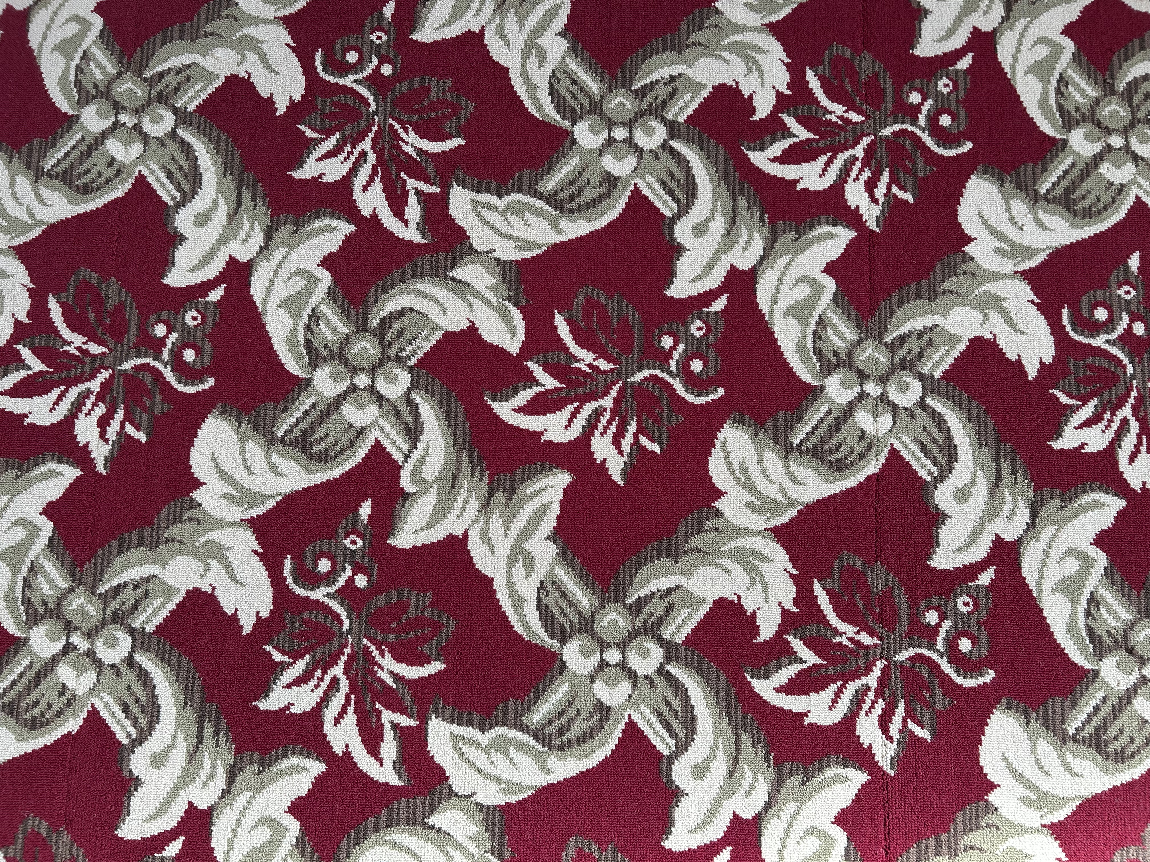 A close up of faded carpet with a green background and gold and red geometric pattern.