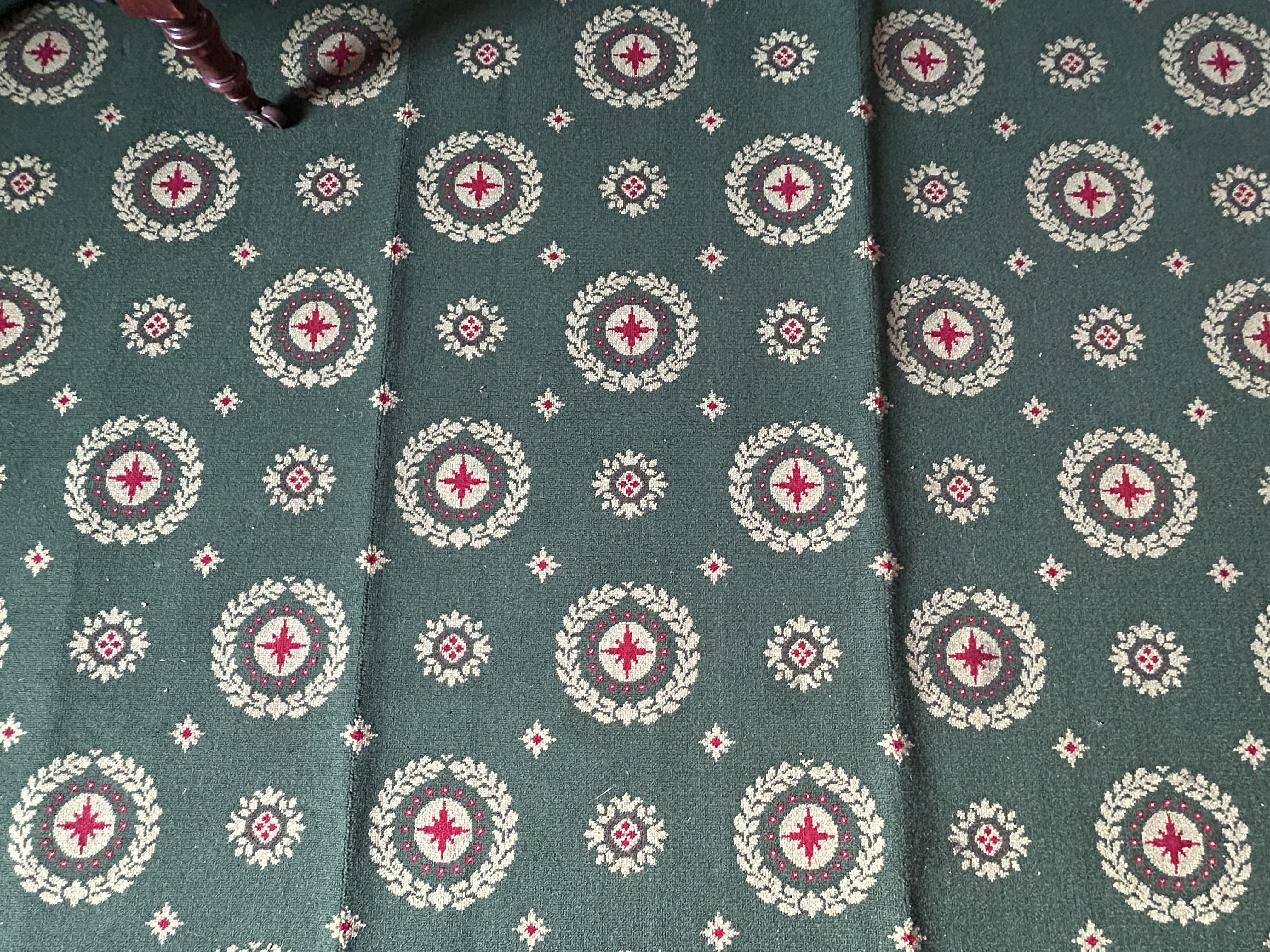 A close up of carpet with a green background and small repeating red pattern. The carpet is rippled due to water damage.