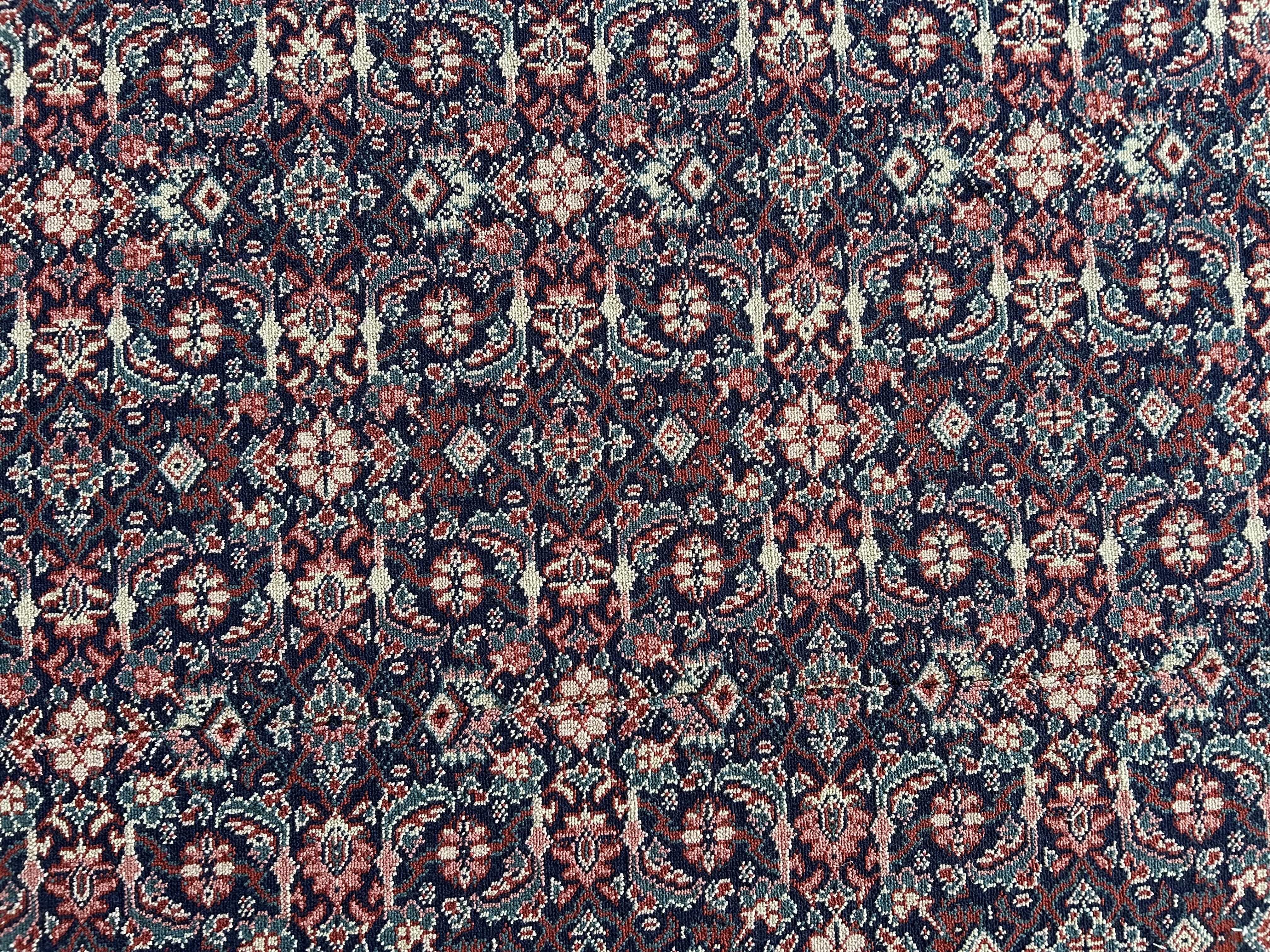 A close up of carpet with a green background and small repeating red pattern. The carpet is rippled due to water damage.