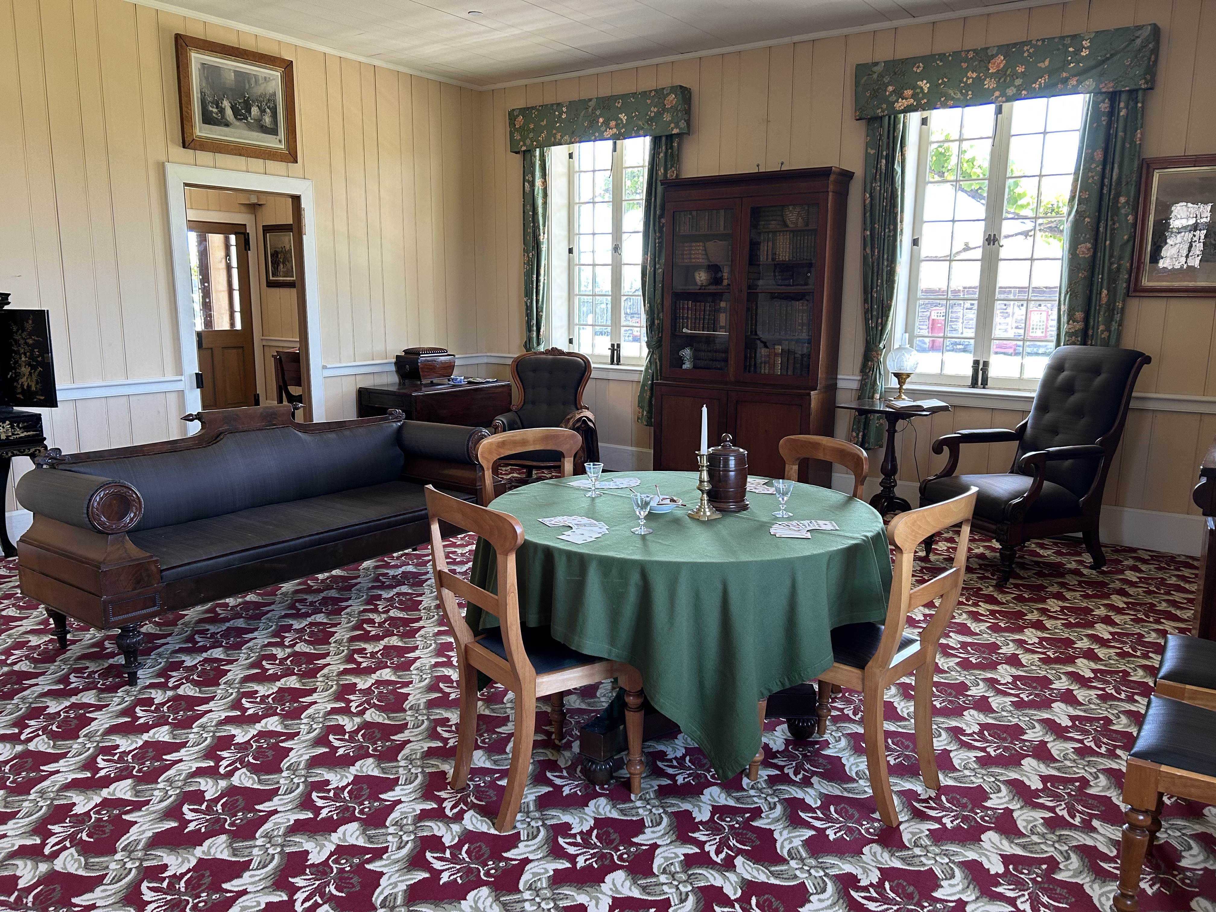 The Douglas Sitting Room in the Chief Factor's House at Fort Vancouver. The room's walls are painted red. Furniture includes a horsehair sofa, table with a tea set, and a bookcase and desk.