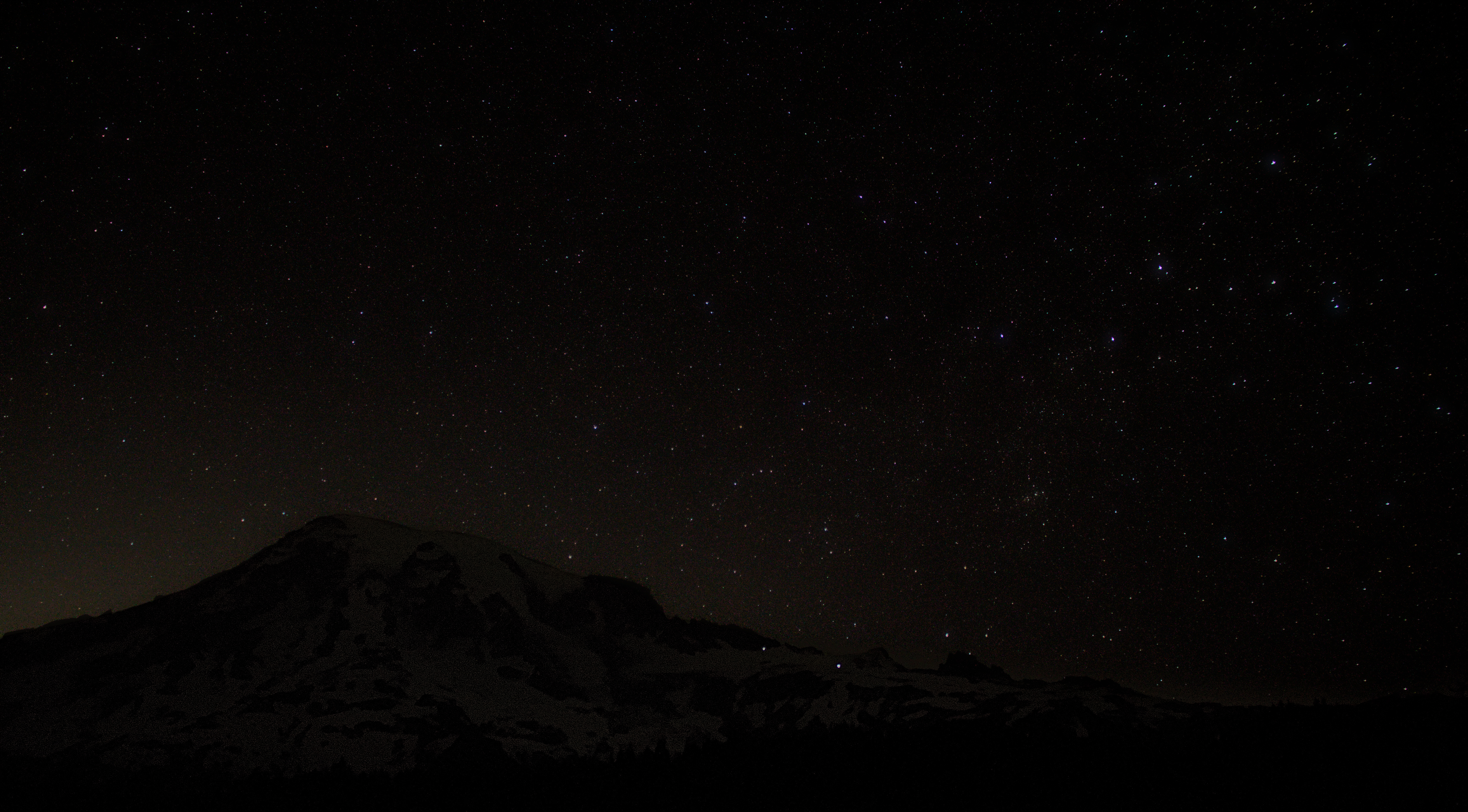 A starry sky above a large volcanic peak.
