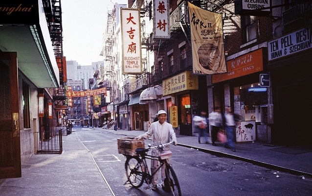 A street in Chinatown with man and bicycle with Chinese businesses and signs in background. 