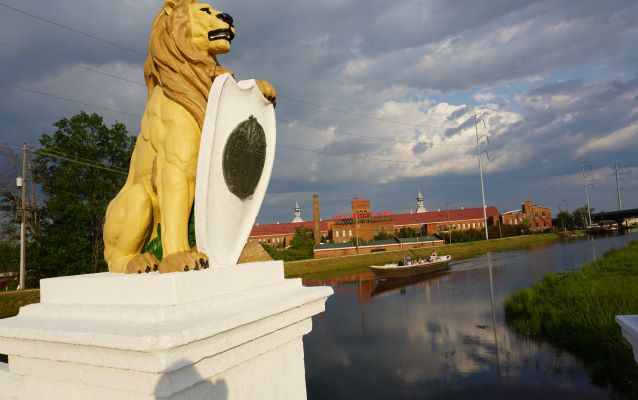 Boat on a canal-way with lion statue in the foreground and buildings in the background. 