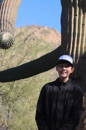 portrait of young man with basecall cap in front of saguaro with arms