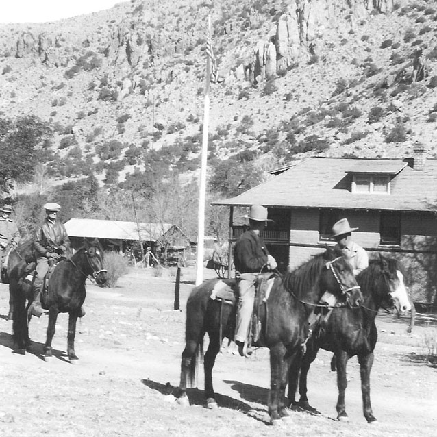 Three people on horses in front of Faraway Ranch buildings