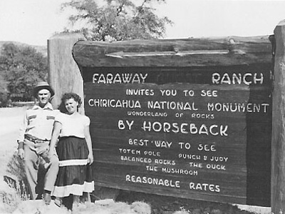 Two visitors pose by a sign for Faraway Ranch advertising trips by horseback to Chiricahua NM