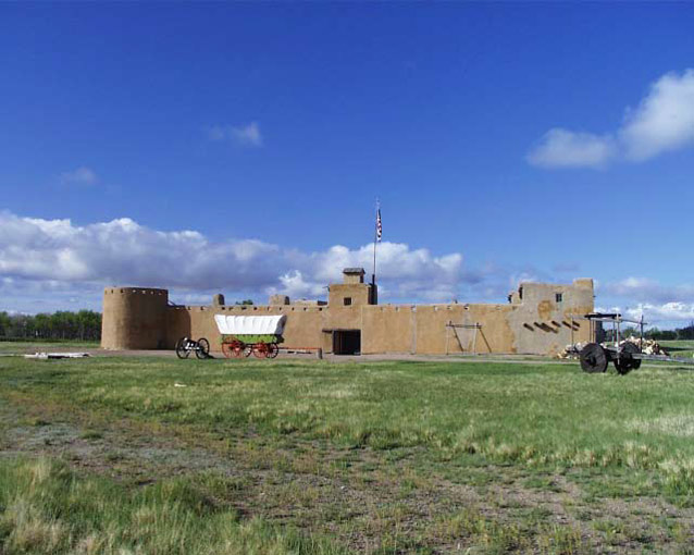 Reconstructed fort in a green, grassy landscape against a blue sky at at Bent’s Old Fort