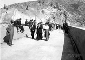 Black and white photo of people walking along the top of the dam