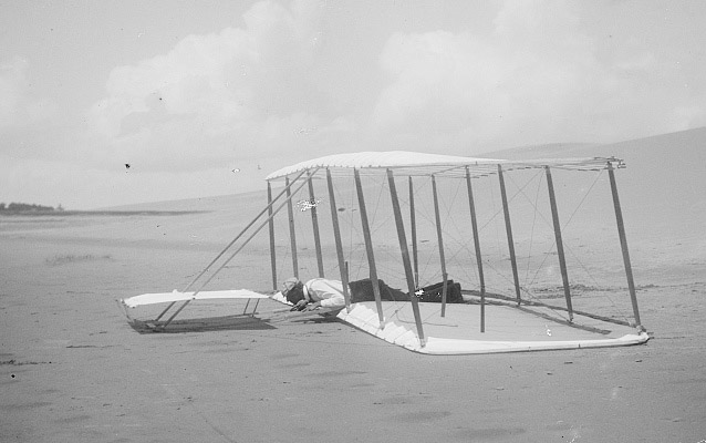 Wilbur laying prone on glider just after landing, skid marks visible on right- Kitty Hawk, 1901