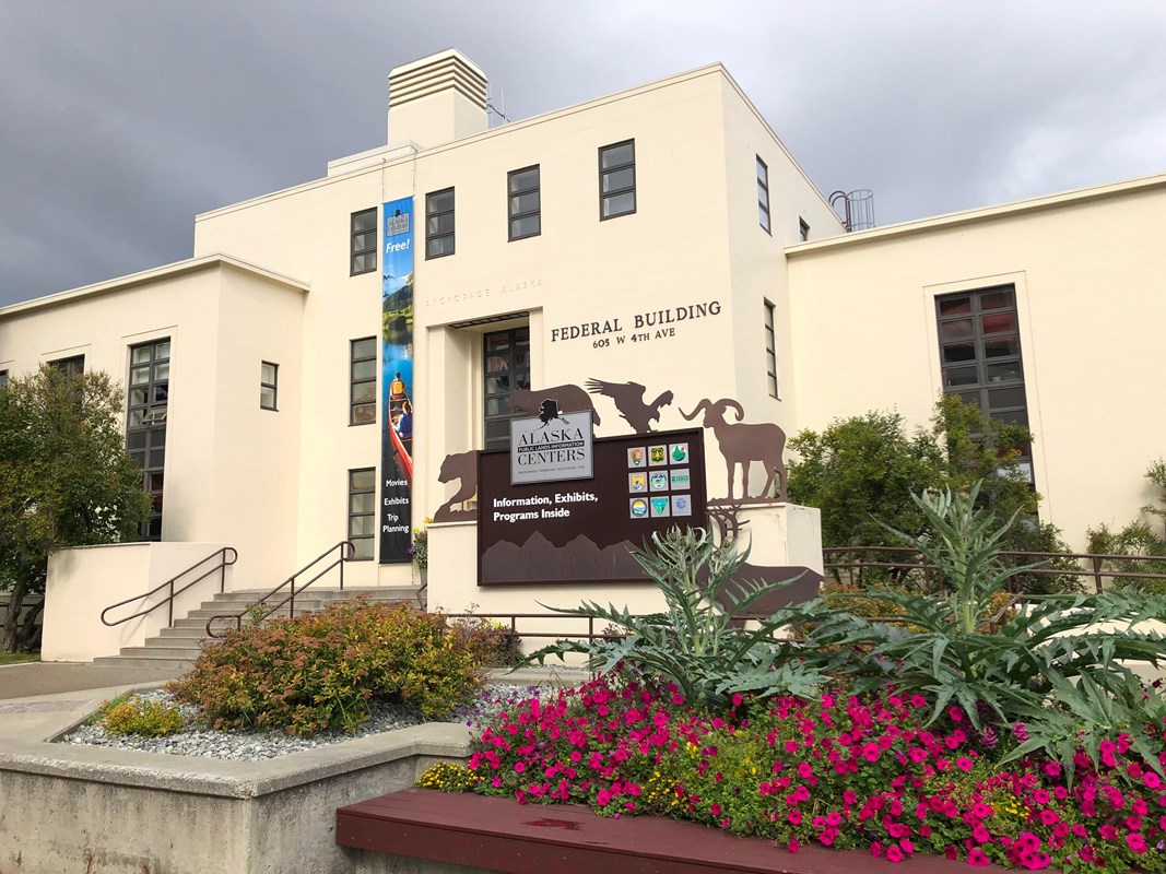 An outdoor view of the Anchorage center, with trees and flowering shrubs in front of the building.