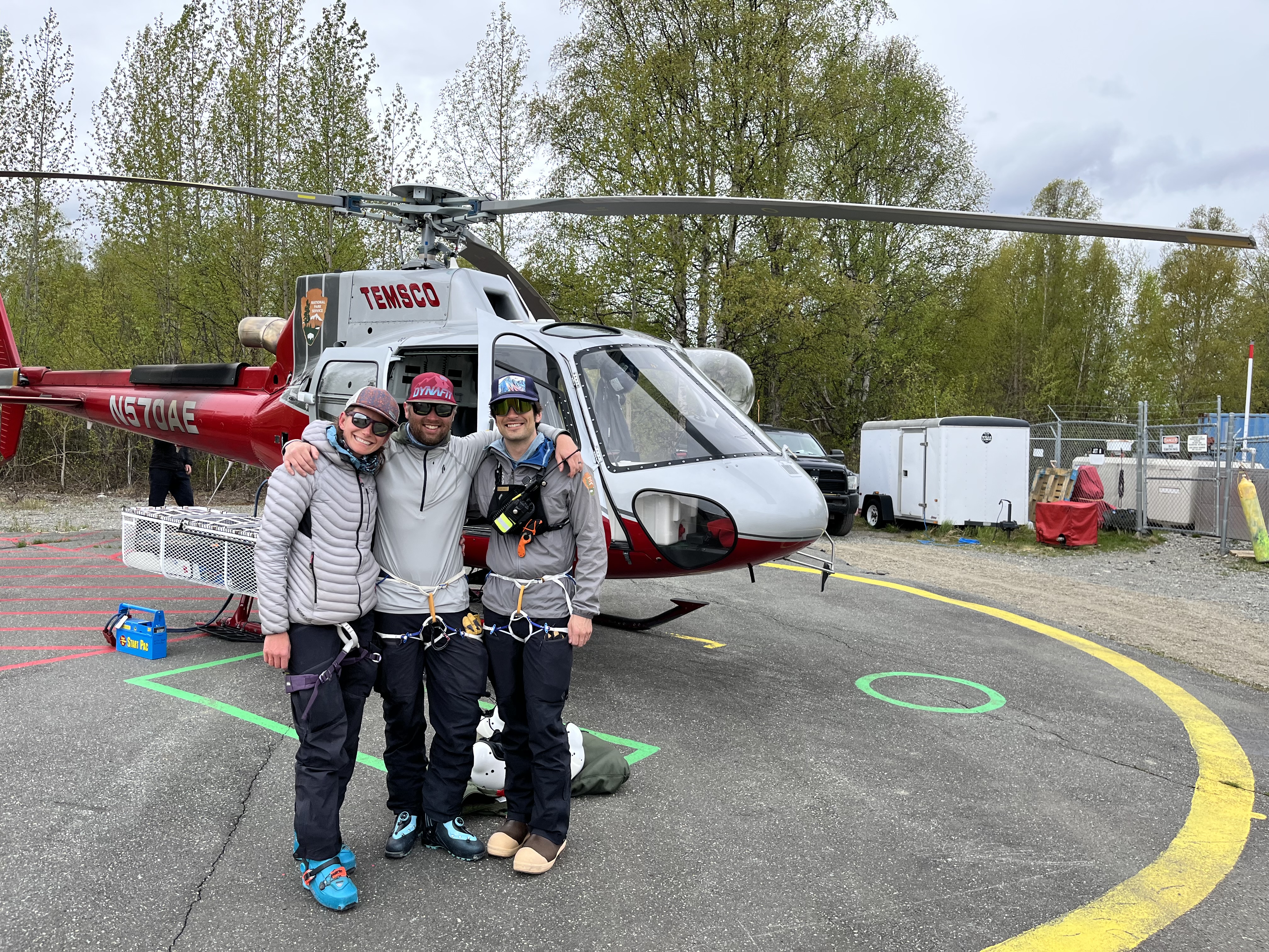 Three mountaineers stand outside a helicopter