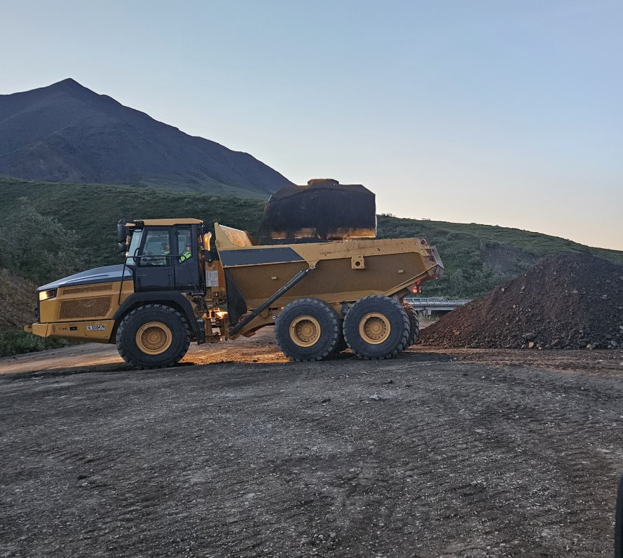Material from a gravel pile is loaded into a dump truck.
