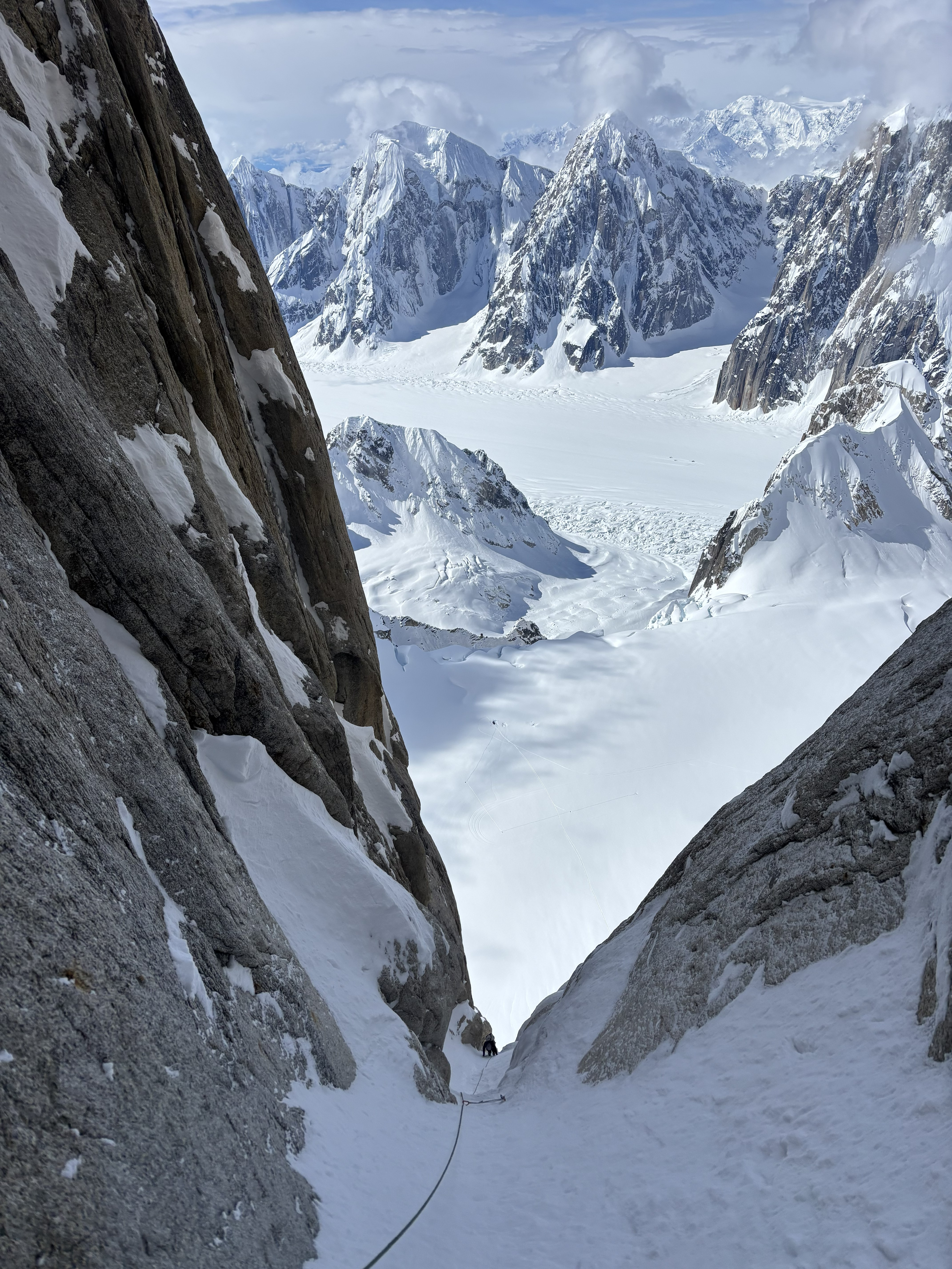 A snow-covered climbing route between to rock walls with a snowy landscape and peaks in the background