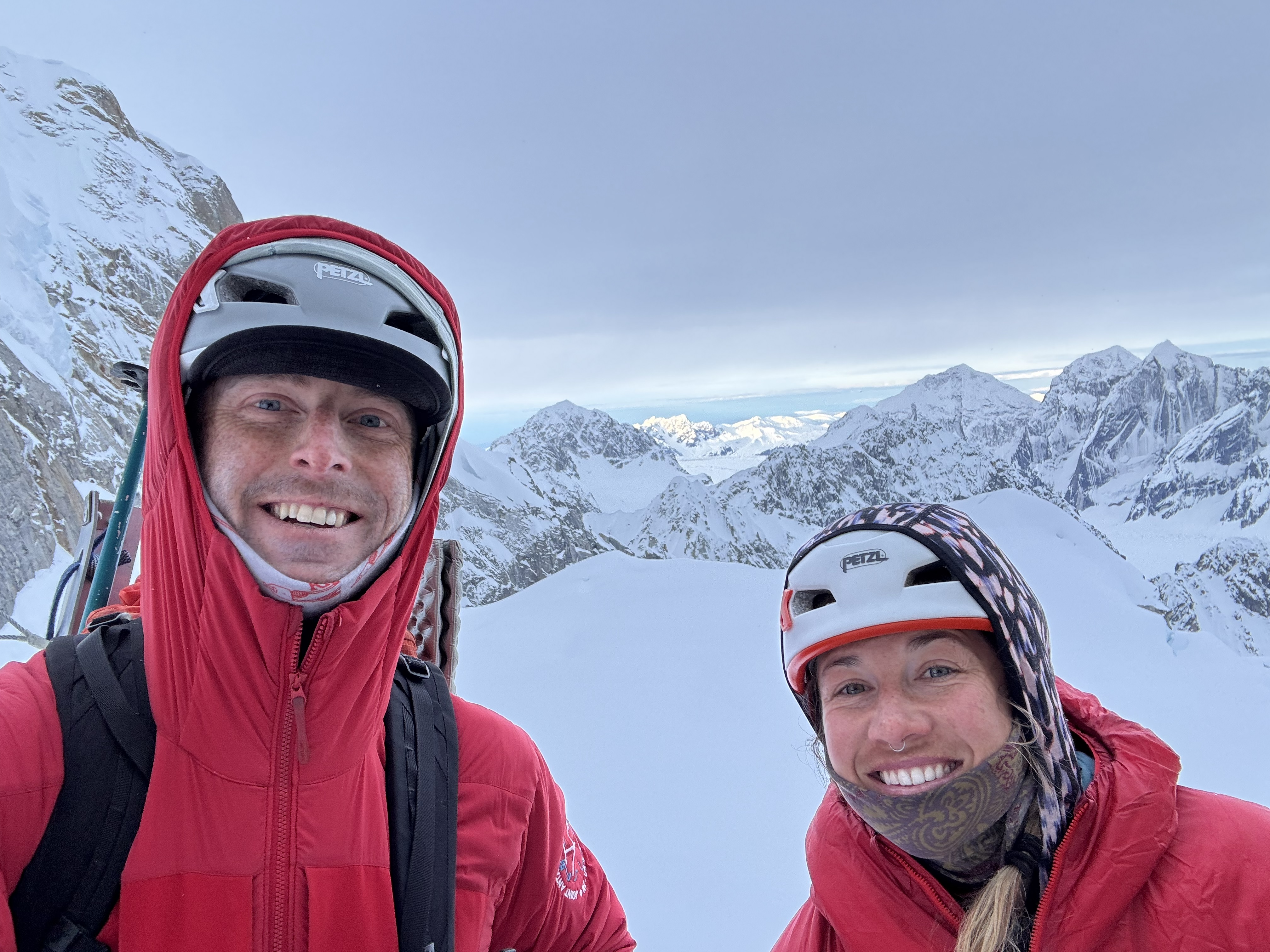 Two smiling climbing rangers in red jackets with snowy peaks in the background