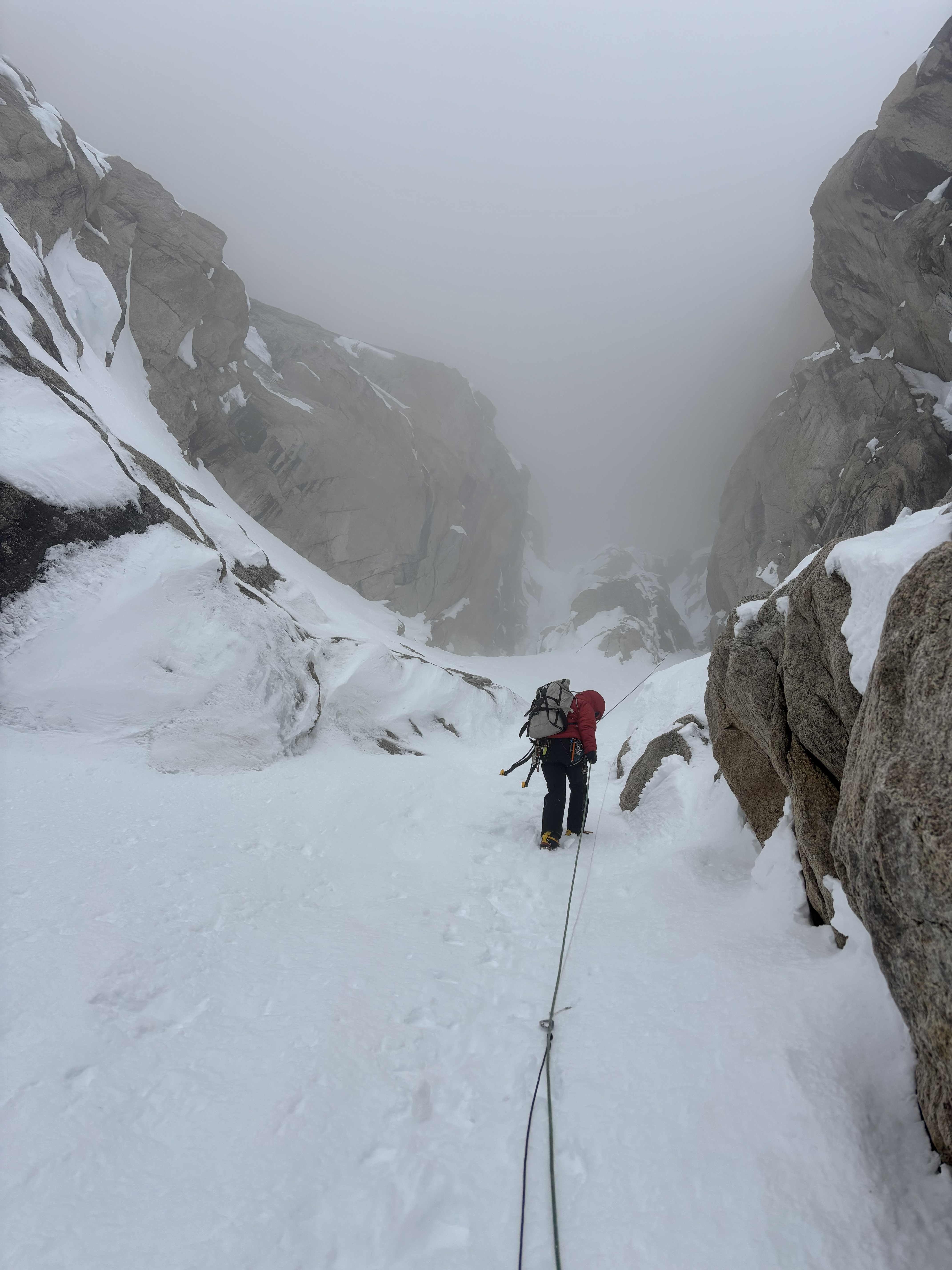 A ranger in a road jacket climbs up a snow-covered pitch facing a foggy section
