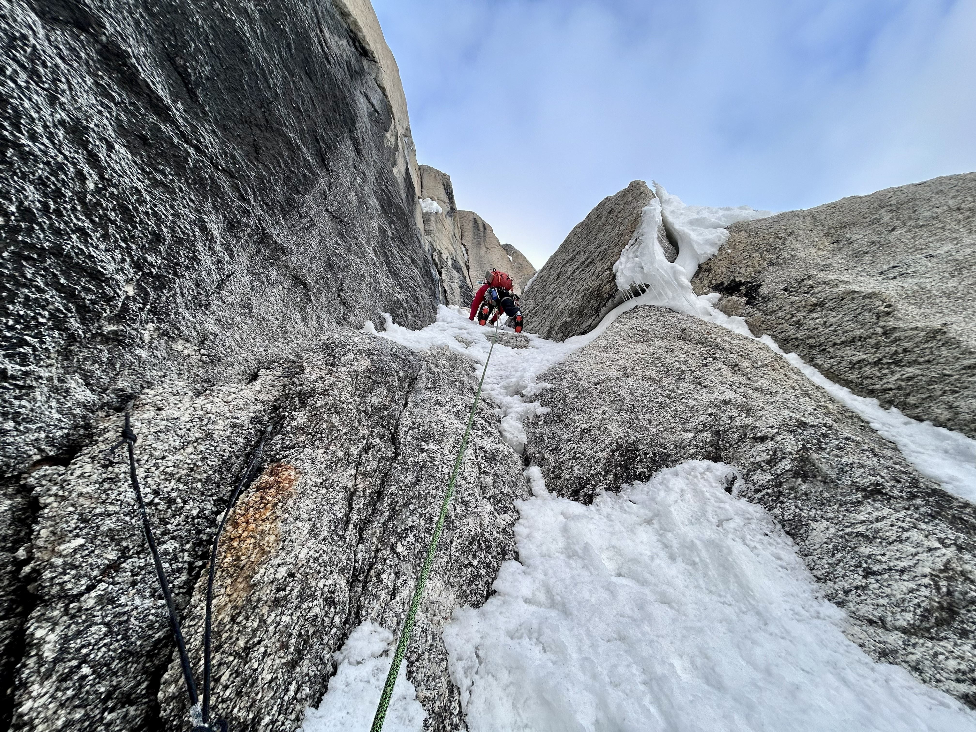 Looking up at a ranger in a red coat climbing up a snowy rock pitch