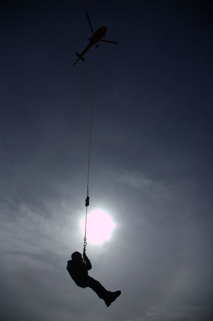 A ranger hangs from a short-haul line under a helicopter. 
