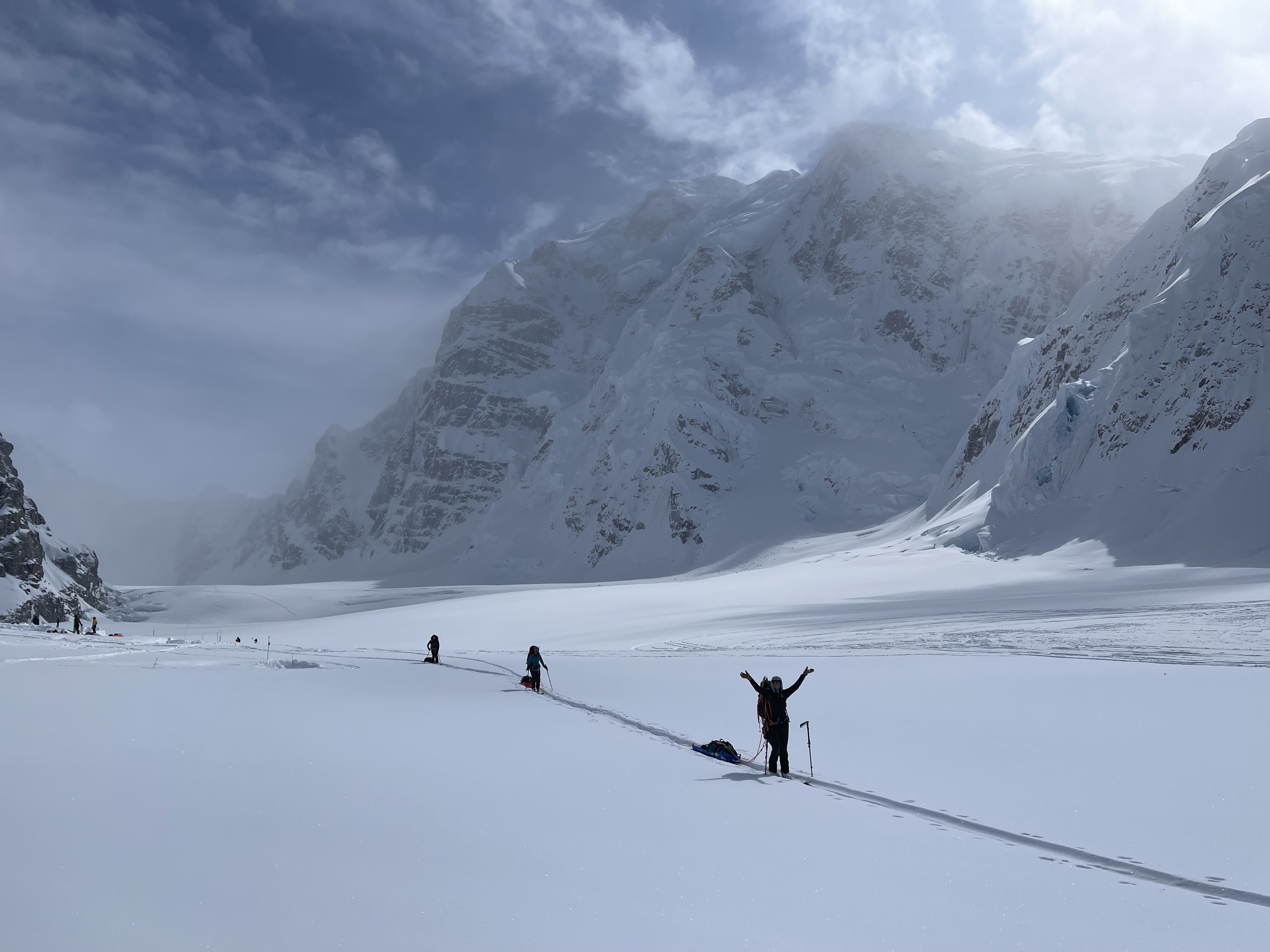 A rope team skis along a flat glacier surrounded by steep mountain peaks