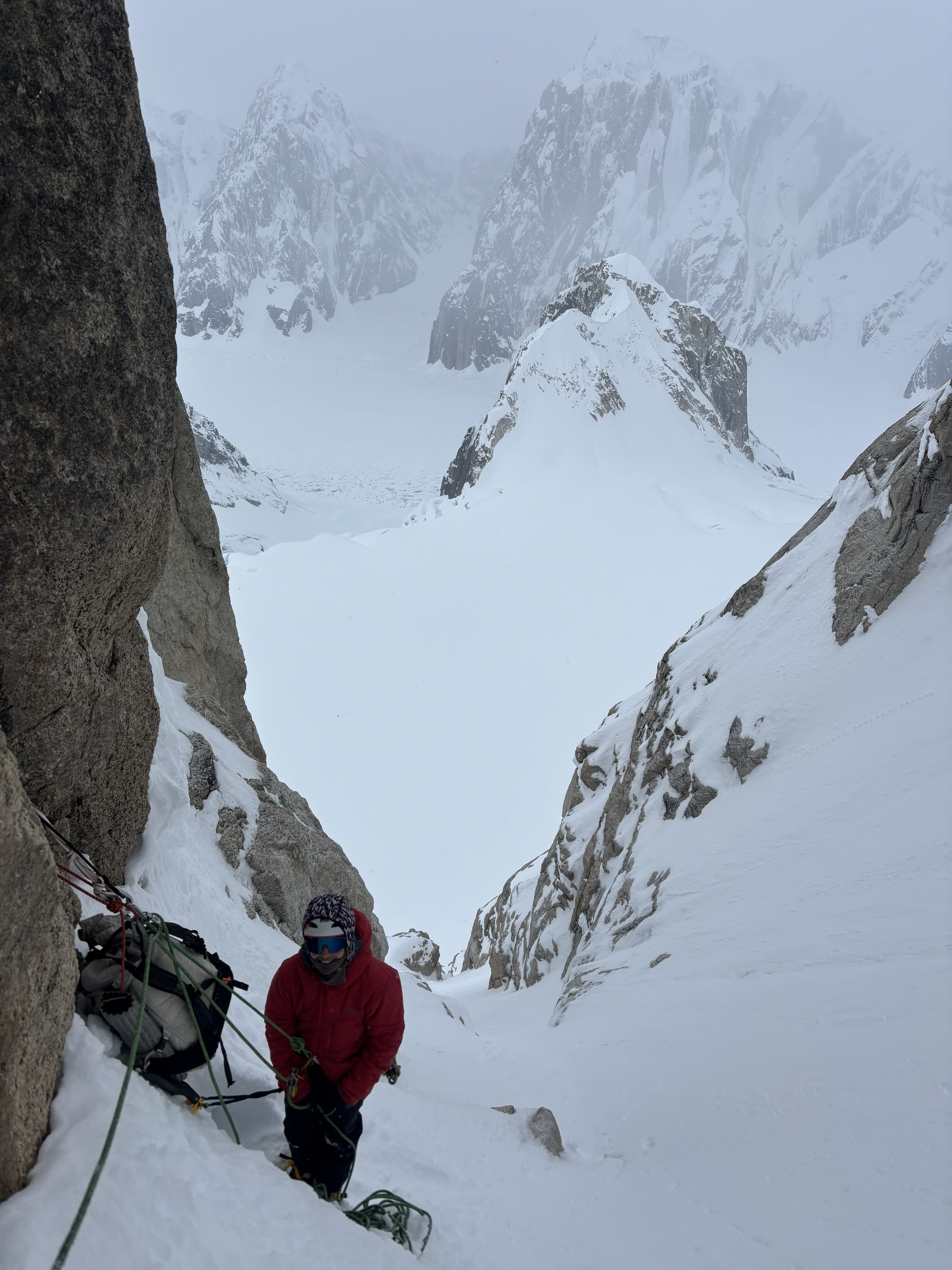 A ranger in a red coat climbing a snowy rock pitch