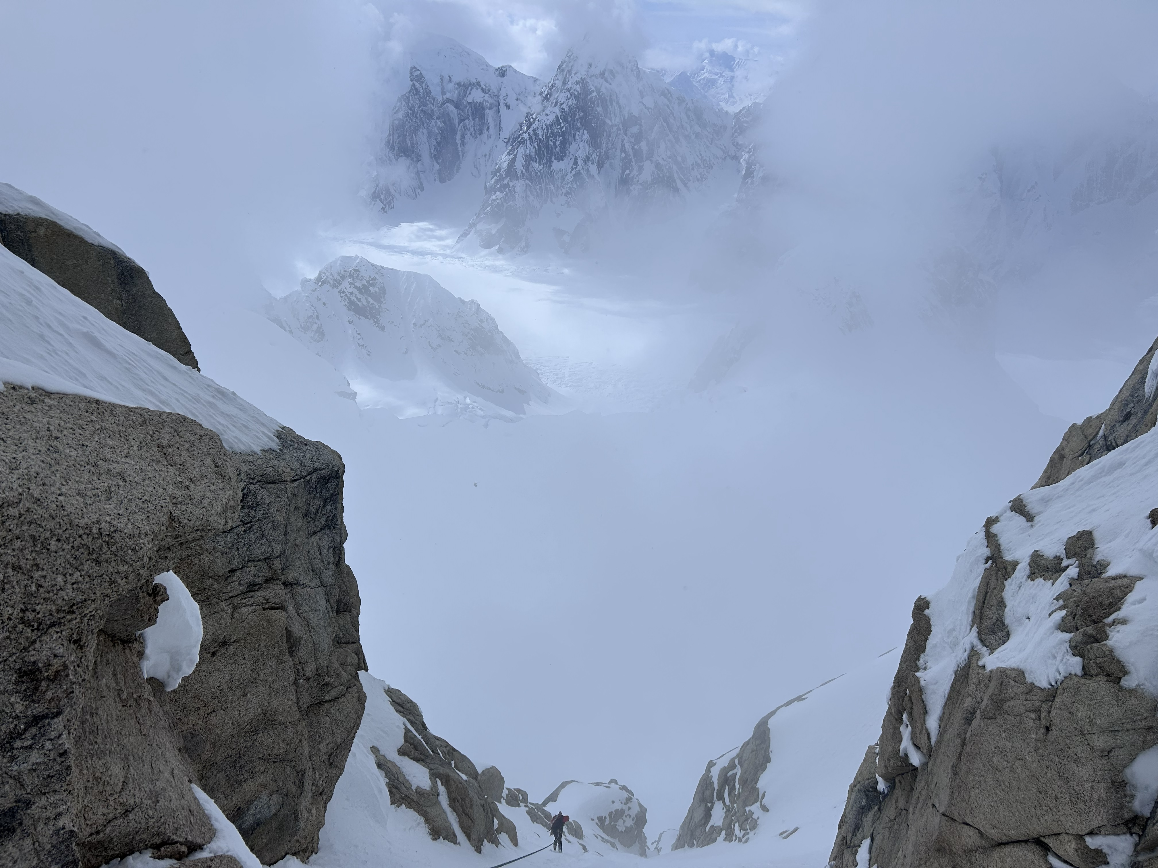 a ranger far in the foreground using fixed anchors to rappel through a snow-covered pitch towards a foggy section