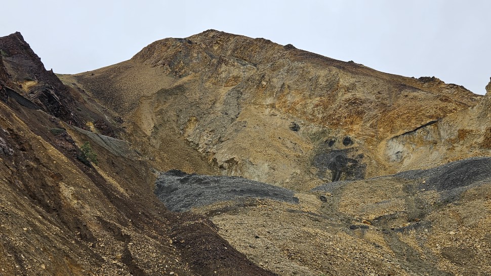 Looking up the landslide, a large section of a rocky mountainside slumps downhill. The flat grade of the road is visible to the left and right of the slump.