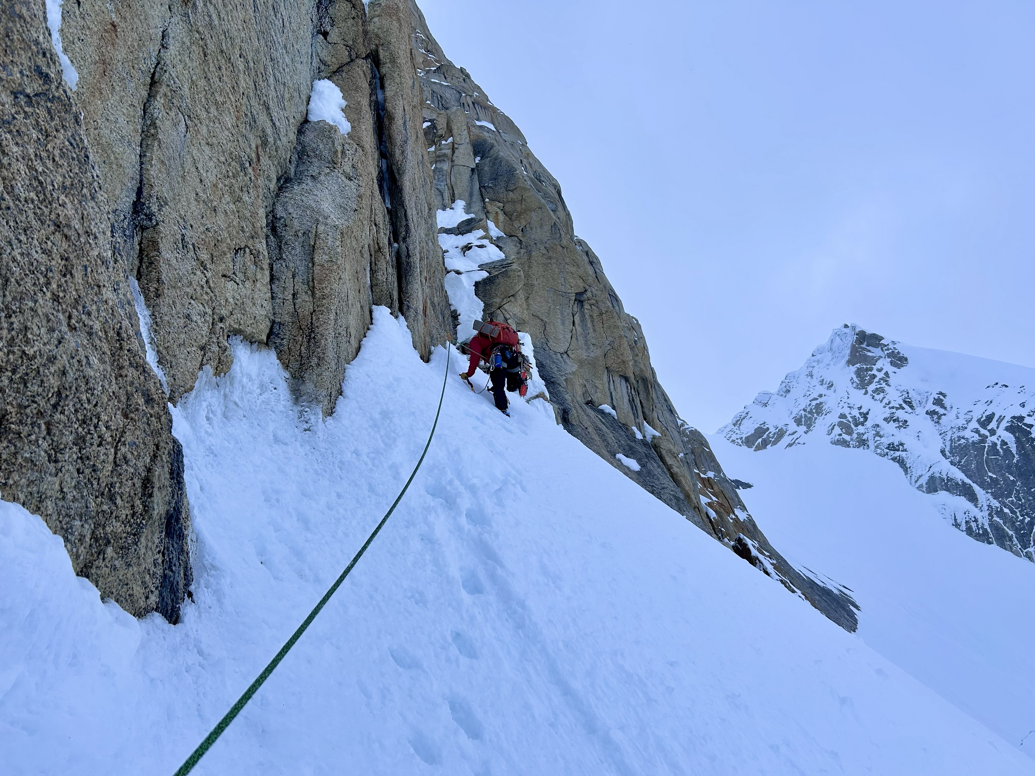 A ranger in a red jacket climbs up a snow-covered pitch