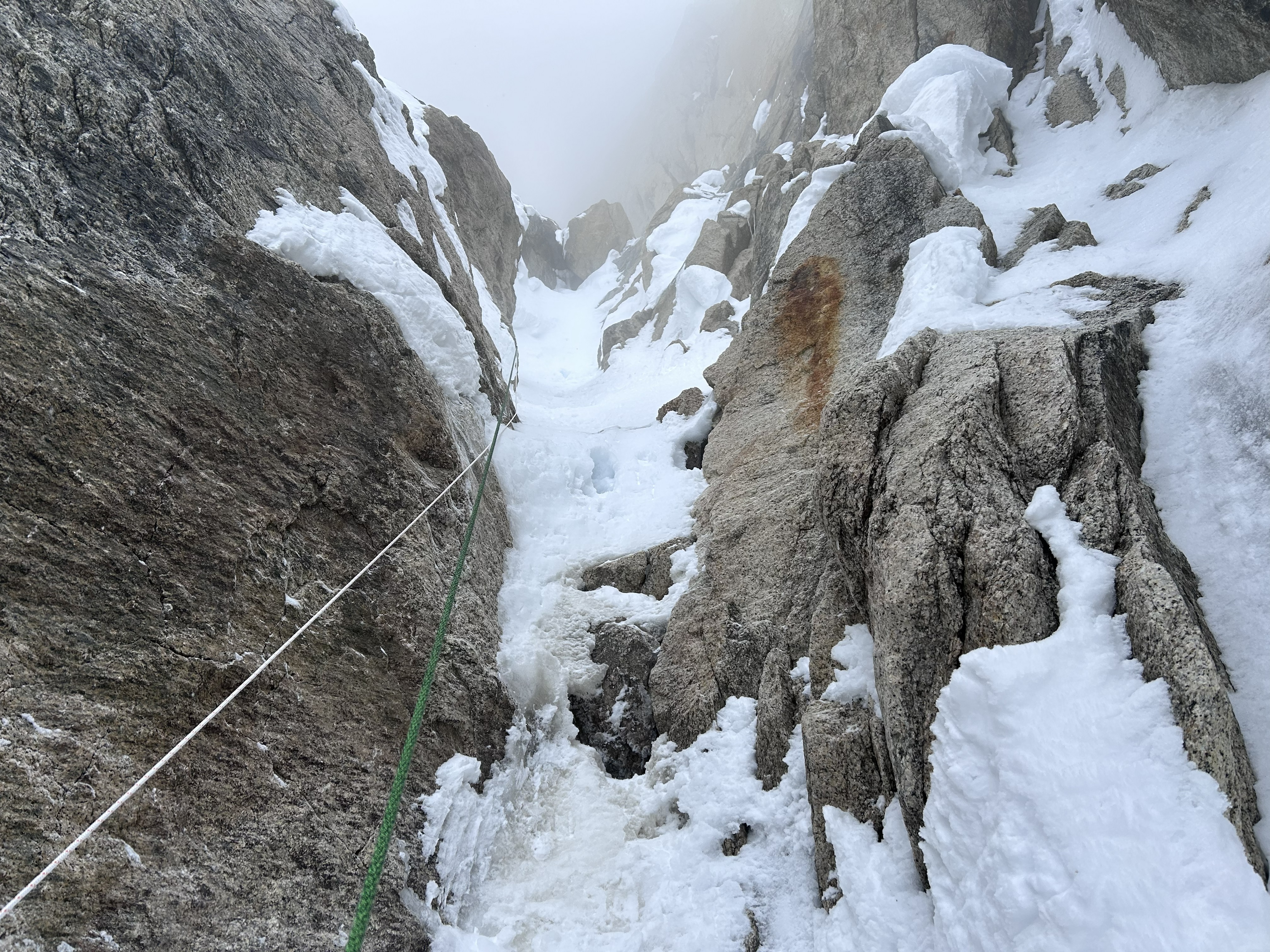 A white rope and green rope hanging down a snowy rock pitch