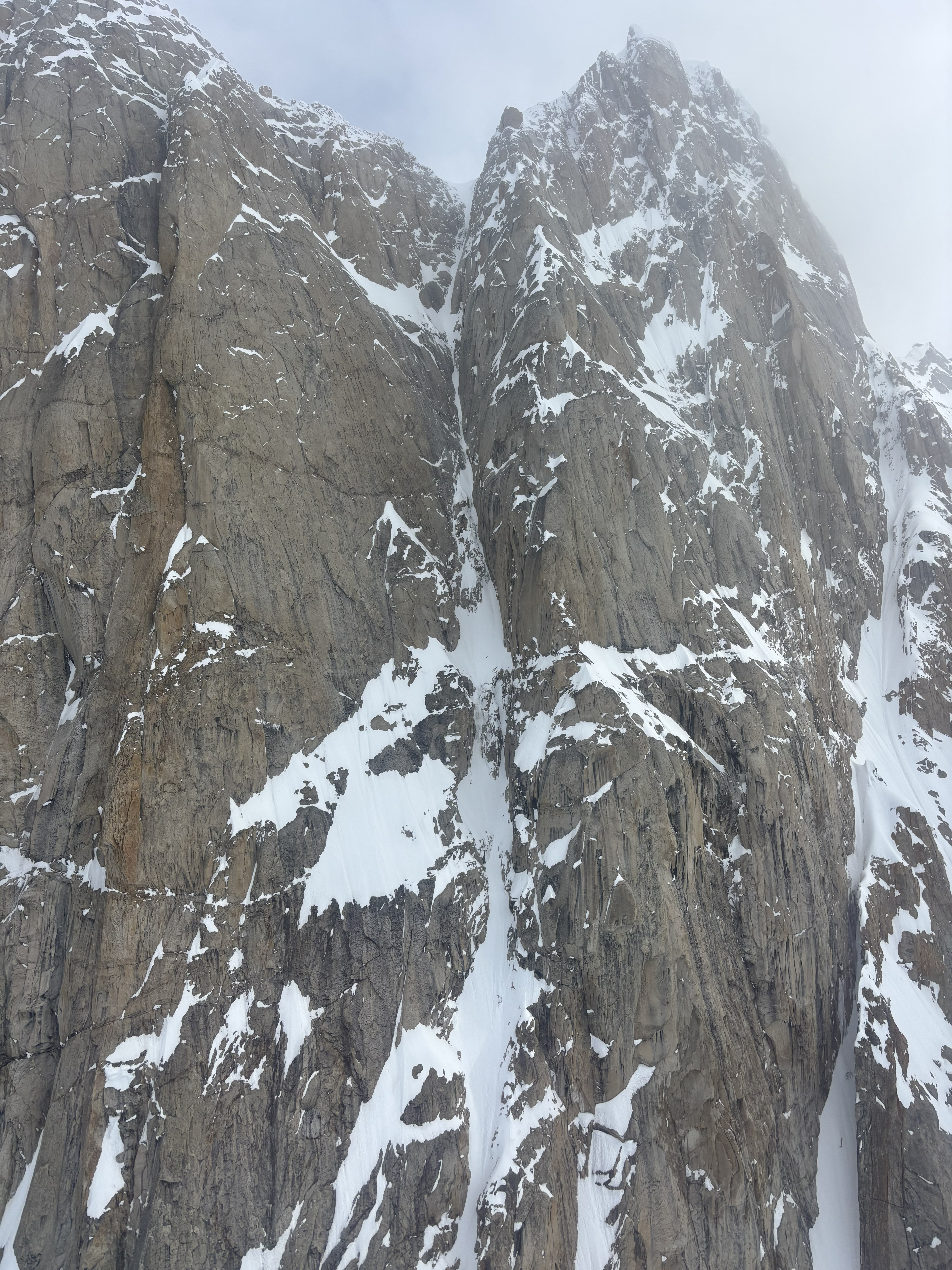 A pitch of snowy rocks ascending toward a grey sky