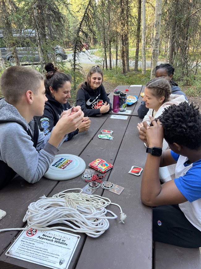 6 people sit around a picnic table playing Uno