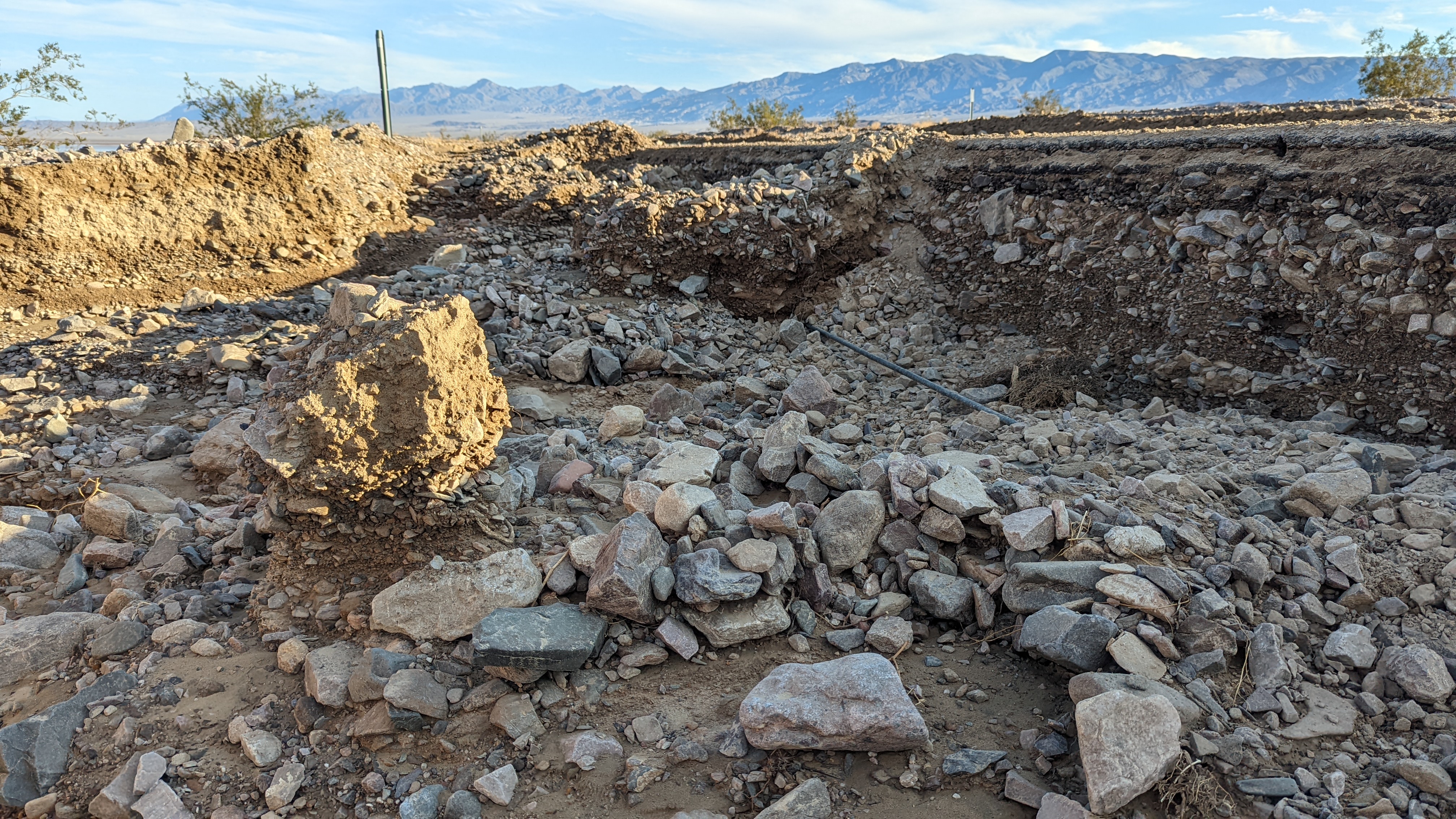 Pictured on the shoulder, asphalt road is undercut from floods leaving rocks and other debris on the steep drop off from original road.