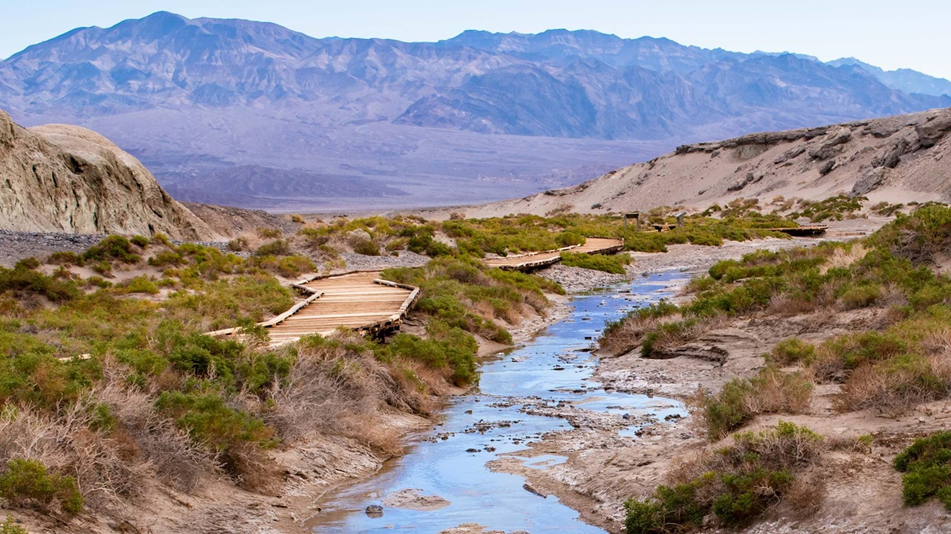 Creek running through canyon area with a boardwalk alongside the stream and mountains in the background.
