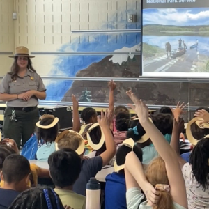 A ranger standing in front of a classroom full of students. Some of those students have their hands up.