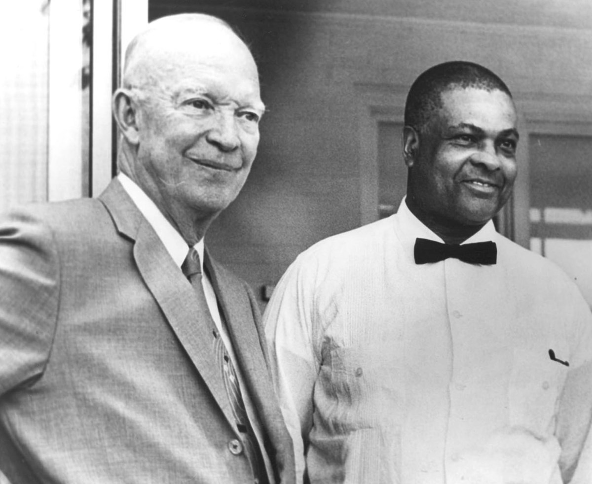Dwight Eisenhower, wearing a grey suit, and John Moaney, wearing a white shirt and black bow tie, smile
