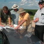 A group of people in bright sunshine look at a trail map