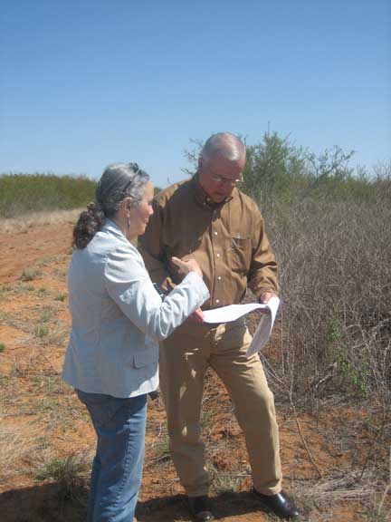 A woman and man are talking and looking at papers outdoors in rural Texas