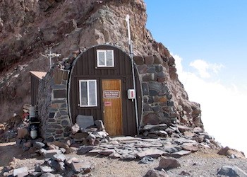 Un pequeño edificio con techo de medio arco hecho de piedra y encaramado en un risco rocoso.
