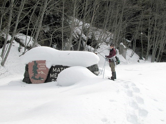 Una excursionista en raquetas de nieve se detiene junto a un letrero cubierto de nieve.
