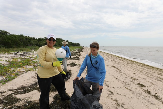A woman and other people standing on a beach, holding trash