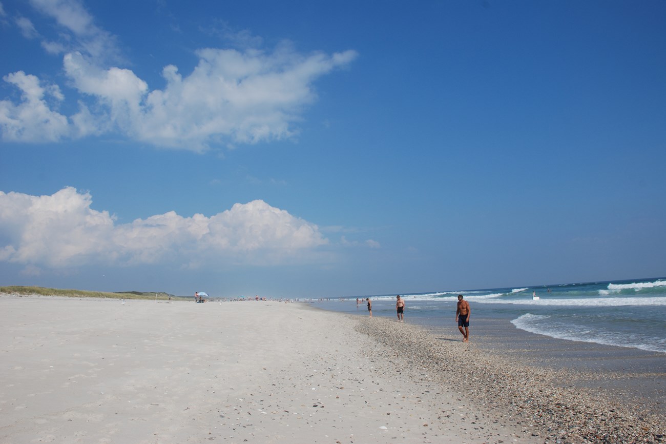 Individuals stroll down quiet wide beach.