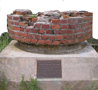 Circular remnant of brick chimney, mounted atop block of granite.