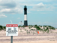Sign on beach in front of lighthouse.