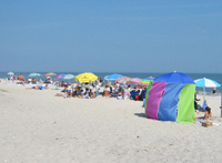 Colorful beach umbrellas and sunshades dot a somewhat crowded beach.
