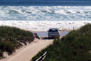 Four-wheel drive vehicle stopped in dune crossing, with waves lapping at the shore.