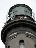 Lighthouse tower tour participants stand along rail of gallery near the top of the Fire Island Lighthouse, under the glass-enclosed lantern room and within the uppermost black daymark of the structure.&nbsp;
