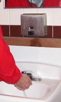 Man in red shirt washes his hands in white sink.