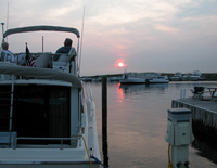 At sunset, a couple relaxing atop a large motor boat watches ferry pull into marina at Watch Hill.