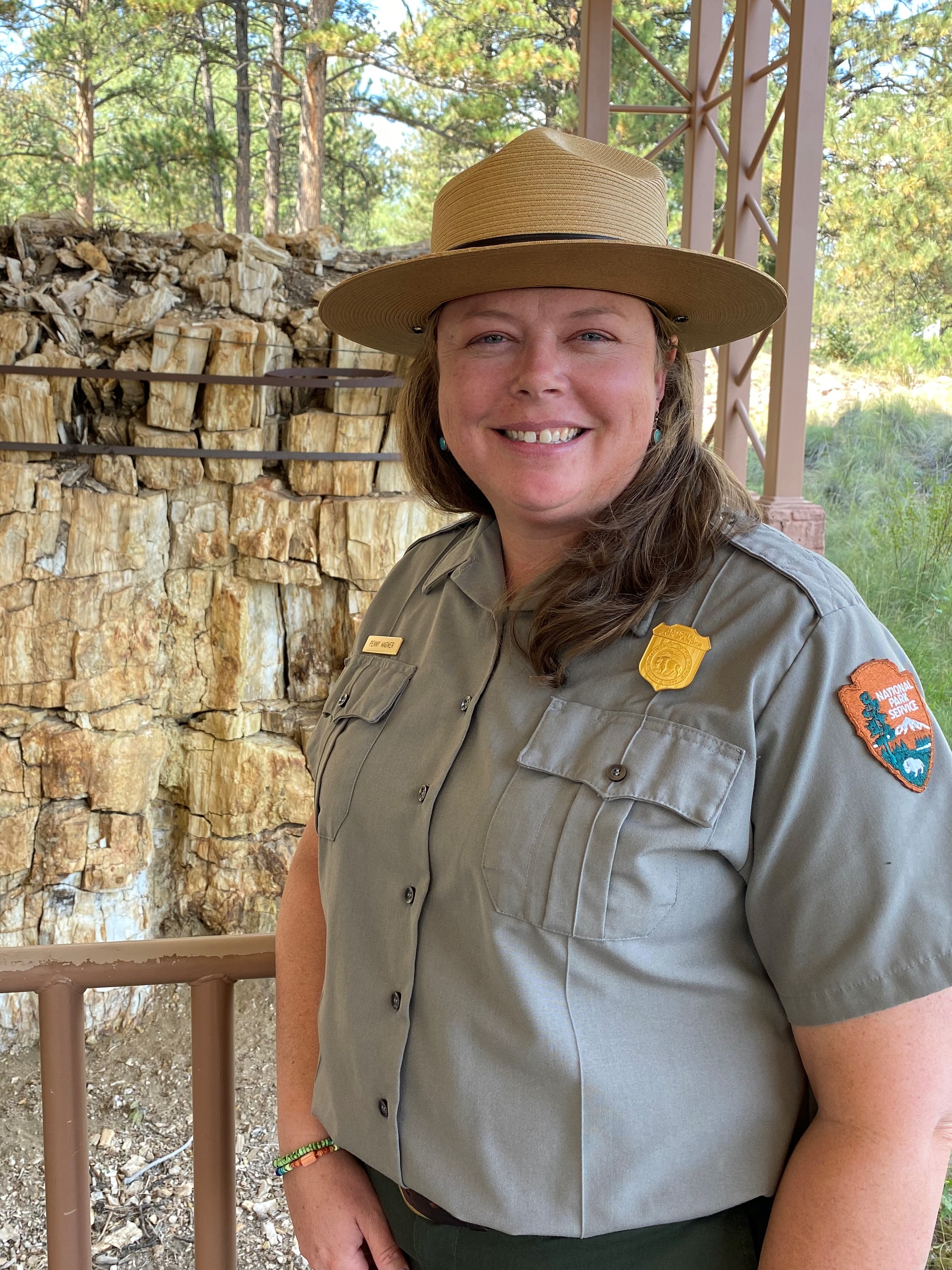 Woman dressed in park ranger uniform with a petrified redwood tree in the background